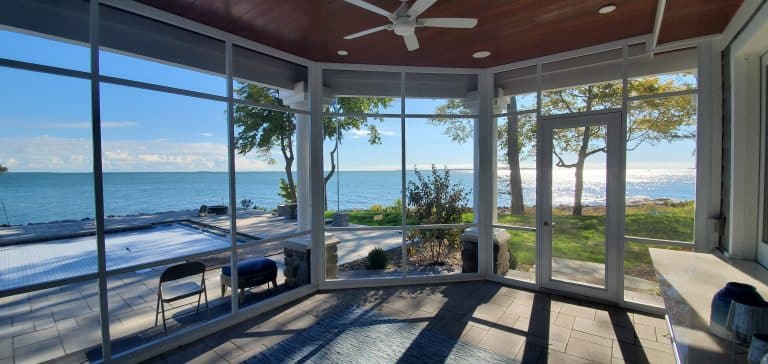 Sunroom with large glass windows overlooking a lake by deck and shade solutions.